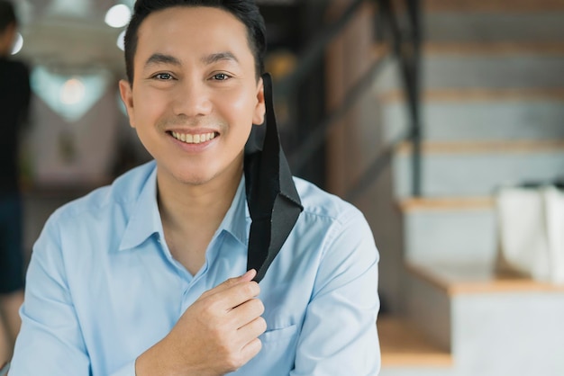 Homme d'affaires asiatique positif enlevant la protection contre les virus du masque facial pour montrer son sourire avec bonne humeur et bien se battre pour propager le concept d'idées de santé épidémique covid 19