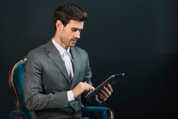 Homme d&#39;affaires assis sur un fauteuil en costume à l&#39;aide d&#39;une tablette numérique sur fond noir