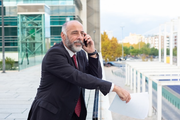 Homme d'affaires aux cheveux gris pensif positif parlant sur téléphone portable