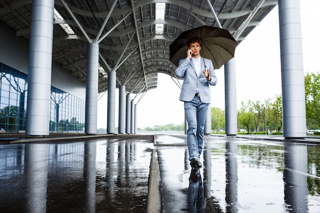 homme d'affaires aux cheveux roux avec parapluie parler au téléphone