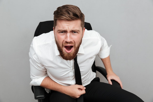 Homme d'affaires barbu frustré assis sur une chaise et à regarder