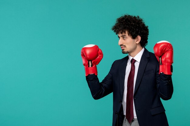 Homme d'affaires beau jeune homme mignon en costume noir et cravate rouge portant des gants de boxe rouges