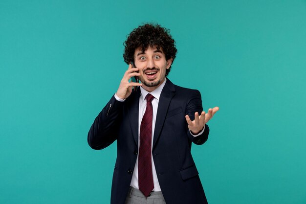 Homme d'affaires bouclé mignon beau mec en costume noir et cravate rouge excité sur l'appel téléphonique