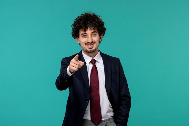 Homme d'affaires bouclé mignon beau mec en costume noir pointant vers l'avant et souriant