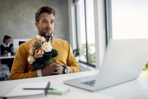 Photo gratuite homme d'affaires avec bouquet de fleurs faisant un appel vidéo sur un ordinateur portable au bureau