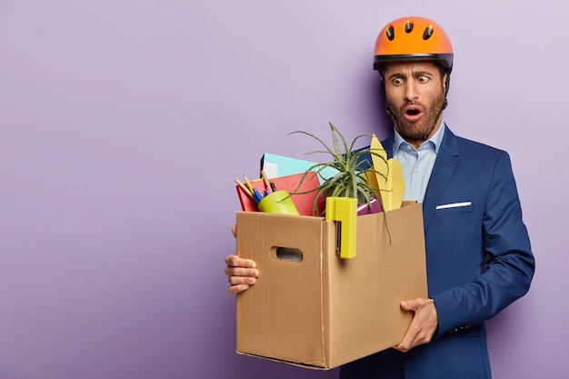 Photo gratuite homme d'affaires choqué posant en costume élégant et casque rouge au bureau