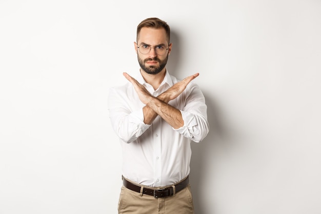 Homme d'affaires en colère fronçant les sourcils et montrant la croix, vous arrêter, dire non et interdire quelque chose, debout