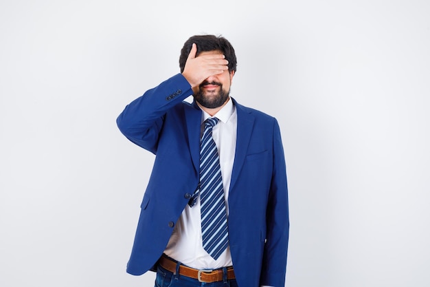 Homme d'affaires en costume formel couvrant les yeux avec la main et l'air sérieux, vue de face.