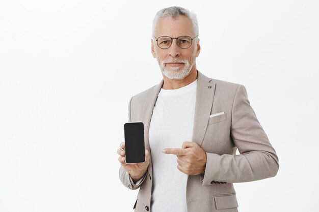 Homme d'affaires en costume et lunettes pointant le doigt sur l'écran du téléphone mobile