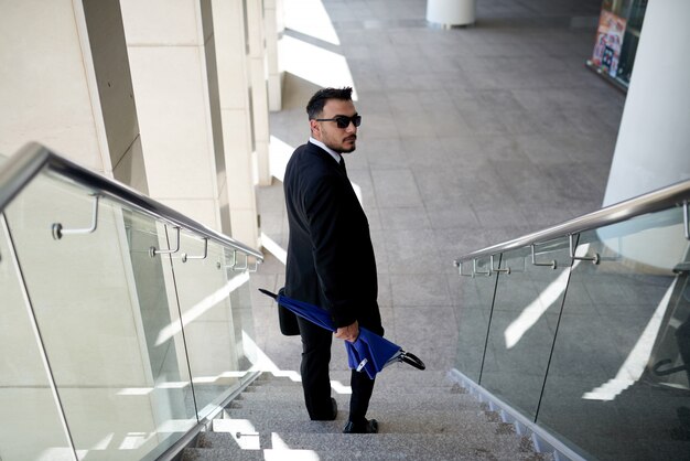 Homme d'affaires en costume et lunettes de soleil en descendant l'escalier et en regardant autour de la caméra