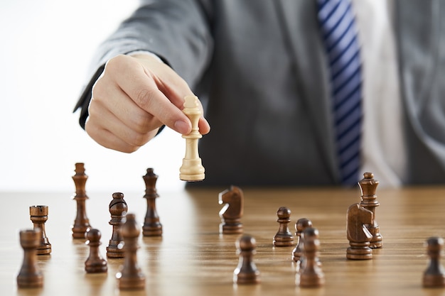 Homme d'affaires en costume utilisant sa pièce d'échecs roi blanc parmi des pièces d'échecs sombres sur une table