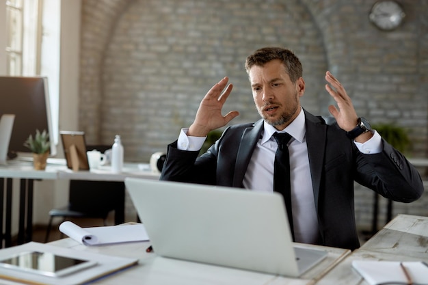 Homme d'affaires désemparé lisant des e-mails problématiques sur un ordinateur portable au bureau