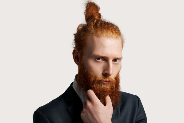 Homme d'affaires efficace et talentueux aux cheveux roux avec une forte vue et tenir sa barbe à la main
