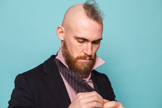 Homme d'affaires européen barbu en costume sombre isolé, noue une cravate