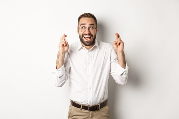 Homme d'affaires excité et plein d'espoir faisant un vœu, croiser les doigts et attendre, debout