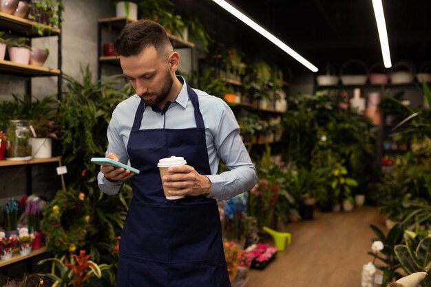 Homme d'affaires fleuriste avec un téléphone à la main et une tasse de café dans un magasin de fleurs et de bouquets
