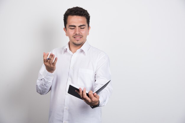 Homme d'affaires fou lisant un cahier sur fond blanc.