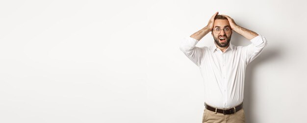 Homme d'affaires frustré tenant les mains sur la tête à l'air choqué et anxieux debout sur fond blanc