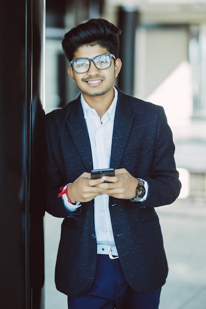 Homme d'affaires indien asiatique textos à l'aide de smartphone en se tenant debout dans le bureau