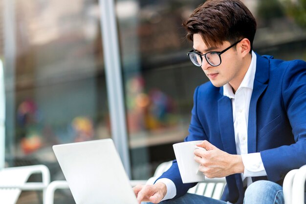 Homme d'affaires intelligent costume formel s'asseoir se détendre main tenir smartphone avec ordinateur portable travail conférence télévidéo réunion travail à distance distance sociale asian ale travail se détendre dans le fond du parc de jardin