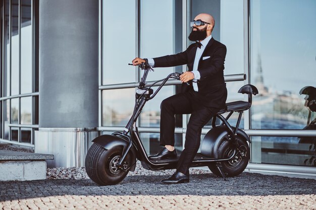 Un homme d'affaires intelligent et séduisant est assis sur son scooter électrique tout en posant pour le photographe.