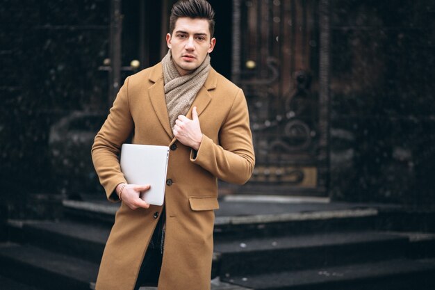 Homme d&#39;affaires jeune en manteau à l&#39;extérieur avec un ordinateur portable