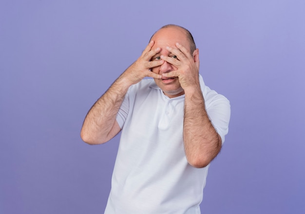 Homme d'affaires mature décontracté mettant les mains sur le visage et regardant la caméra à travers les doigts isolés sur fond violet avec espace copie