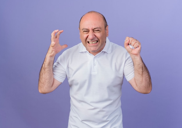 Homme d'affaires mature occasionnel en colère gardant la main dans l'air et papier écrasant avec main isolé sur fond violet
