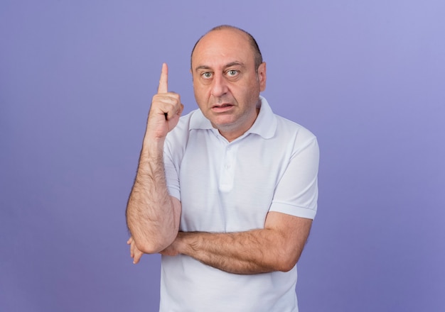 Homme d'affaires mature occasionnel impressionné mettant la main sous le coude et levant le doigt isolé sur fond violet avec espace de copie