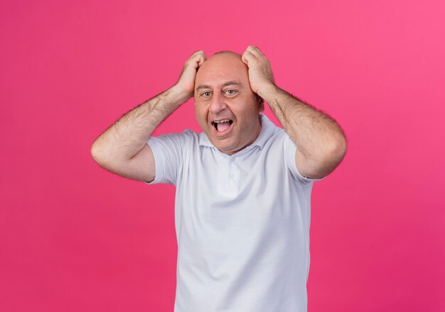 Homme d'affaires mature occasionnel impressionné mettant les mains sur la tête en regardant la caméra isolée sur fond rose