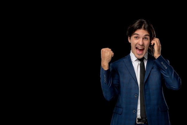 Homme d'affaires mignon beau mec en costume bleu foncé avec la cravate excité tenant les poings et le téléphone