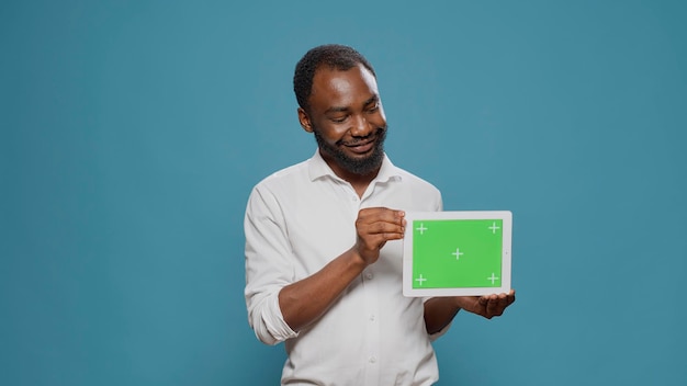 Homme d'affaires montrant un écran vert horizontal sur tablette numérique en studio. Jeune adulte tenant un appareil moderne avec clé chroma vierge, arrière-plan de maquette isolé et modèle d'espace de copie.