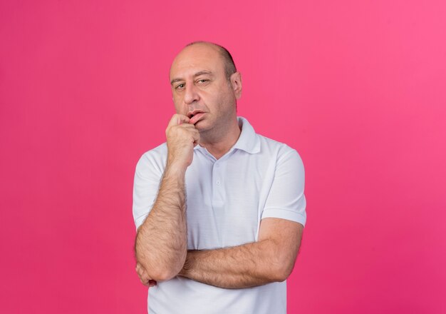 Homme d'affaires mûr occasionnel réfléchi debout avec une posture fermée et mettant le doigt sur la lèvre isolé sur fond rose avec espace de copie