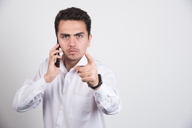 Homme d'affaires parlant avec téléphone portable et pointant la caméra sur fond blanc.