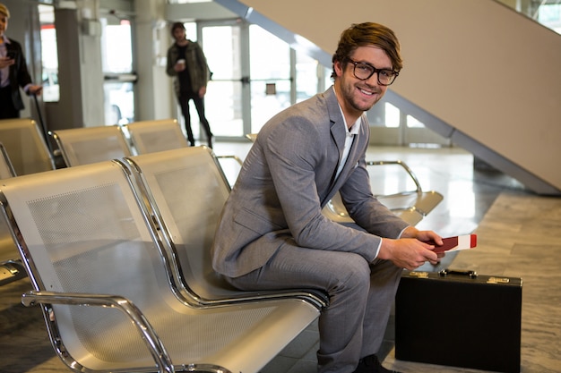 Photo gratuite homme d'affaires avec passeport, carte d'embarquement et mallette assis dans la zone d'attente