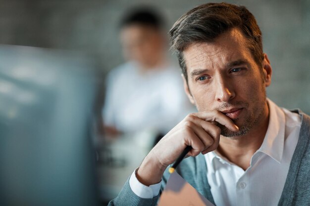 Homme d'affaires pensif lisant quelque chose sur l'ordinateur au bureau