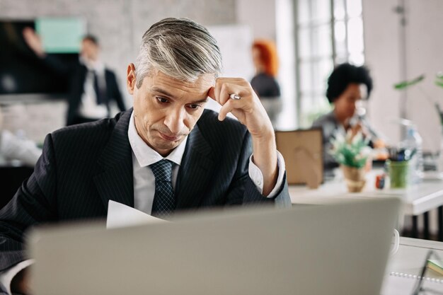 Homme d'affaires pensif pensant comment résoudre les problèmes tout en faisant de la paperasse au bureau Il y a des gens en arrière-plan