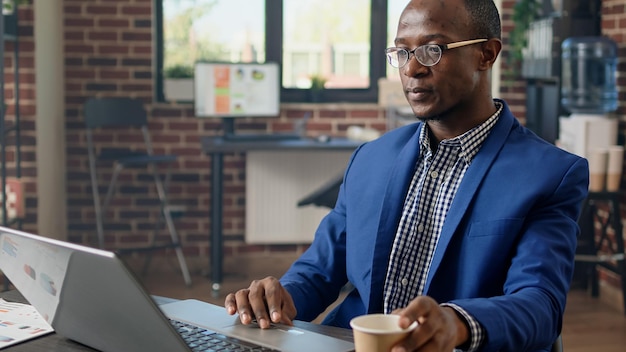 Homme d'affaires planifiant une stratégie financière dans un bureau de mur de briques, travaillant sur un travail de démarrage. Chef de projet utilisant des statistiques pour trouver des informations pour un projet d'entreprise sur un navigateur Web. Prise de vue à main levée.