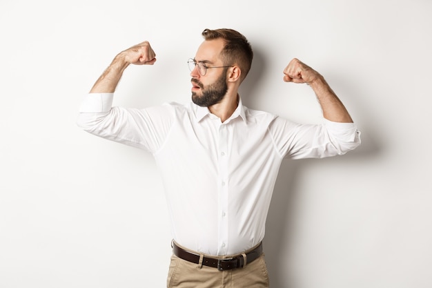 Homme d'affaires prospère flex biceps, montrant les muscles et l'air confiant, se sentant fort, debout.