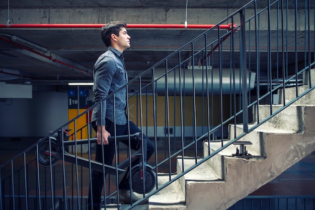 Homme d'affaires prospère à monter les escaliers du bâtiment allant au bureau de travail tout en tenant un scooter électrique pour les déplacements