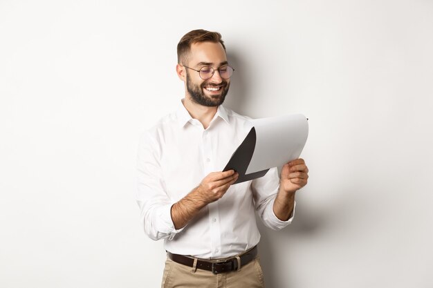 Homme d'affaires à la recherche de documents satisfaits, rapport de lecture et souriant, debout