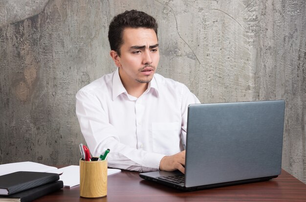 Homme d'affaires à la recherche d'un ordinateur portable et assis au bureau. Photo de haute qualité