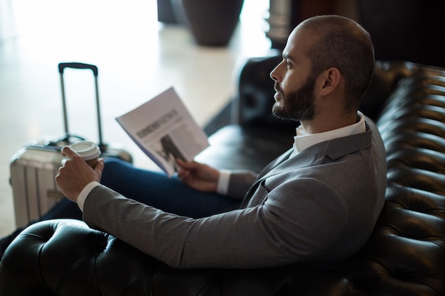 Homme d'affaires réfléchi tenant un journal et une tasse de café dans la zone d'attente