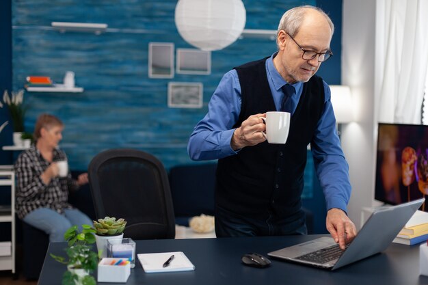 Homme d'affaires à la retraite allumant un ordinateur portable en dégustant une tasse de café