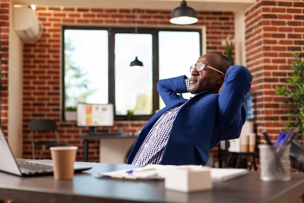 Homme d'affaires se relaxant après avoir terminé la tâche, prenant une pause dans le bureau de démarrage. Employé se sentant insouciant, assis avec les mains au-dessus de la tête pour se détendre et rêvasser une fois le travail terminé. Adulte paisible