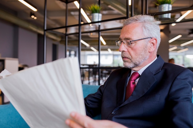 Photo gratuite homme d'affaires senior assis en lisant un journal au bureau