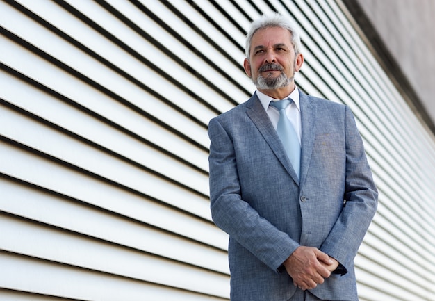 Photo gratuite homme d'affaires senior avec les bras croisés à l'extérieur du bâtiment de bureau moderne.