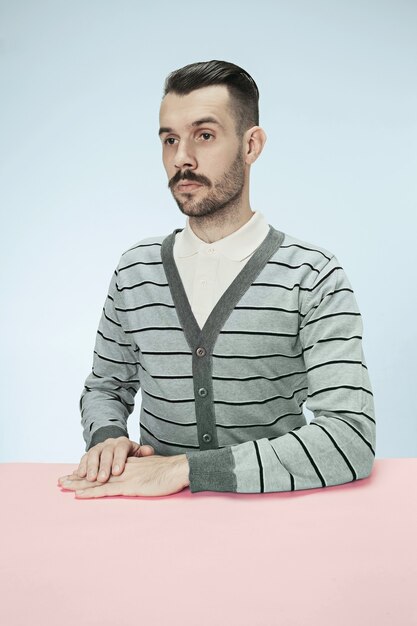 Homme d'affaires sérieux assis à table sur fond de studio bleu. Le portrait dans un style minimalisme