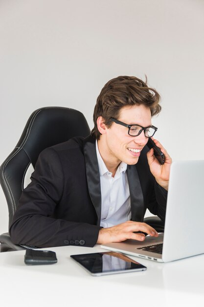 Homme d&#39;affaires souriant à l&#39;aide d&#39;un ordinateur portable tout en parlant sur smartphone