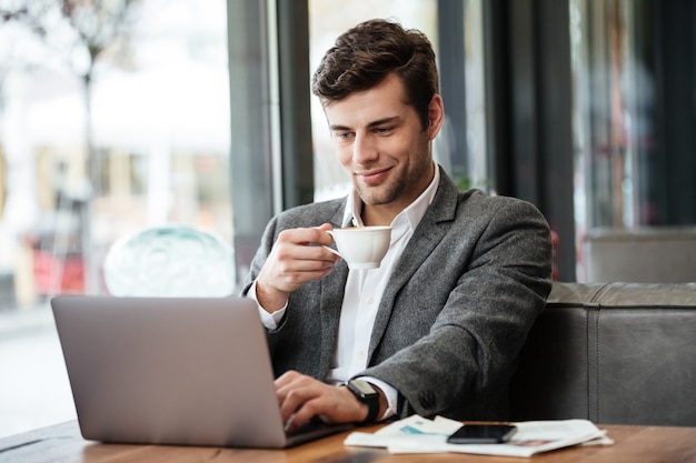 Homme d'affaires souriant assis près de la table au café et à l'aide d'un ordinateur portable